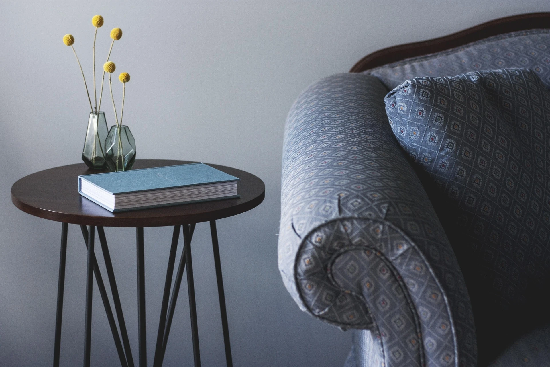 Close-up of a patterned sofa, blue book, and decorative vases on a modern round side table in a contemporary living room.